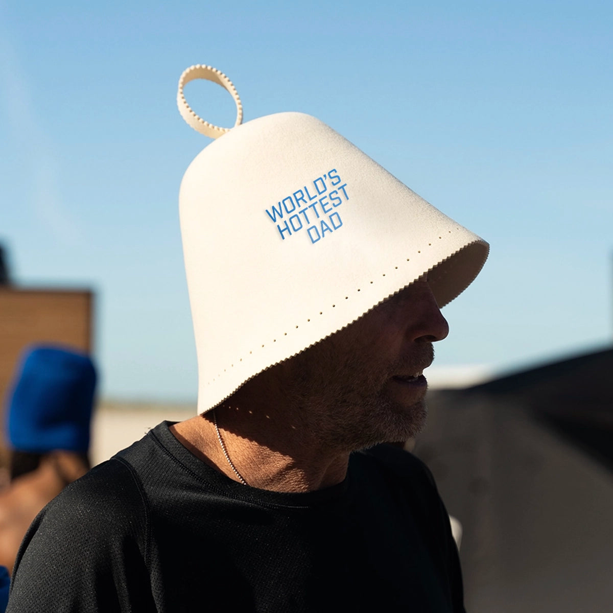 Dad wearing “World’s Hottest Dad” wool sauna hat during backyard sauna session — cozy, insulating headwear with playful embroidered slogan
