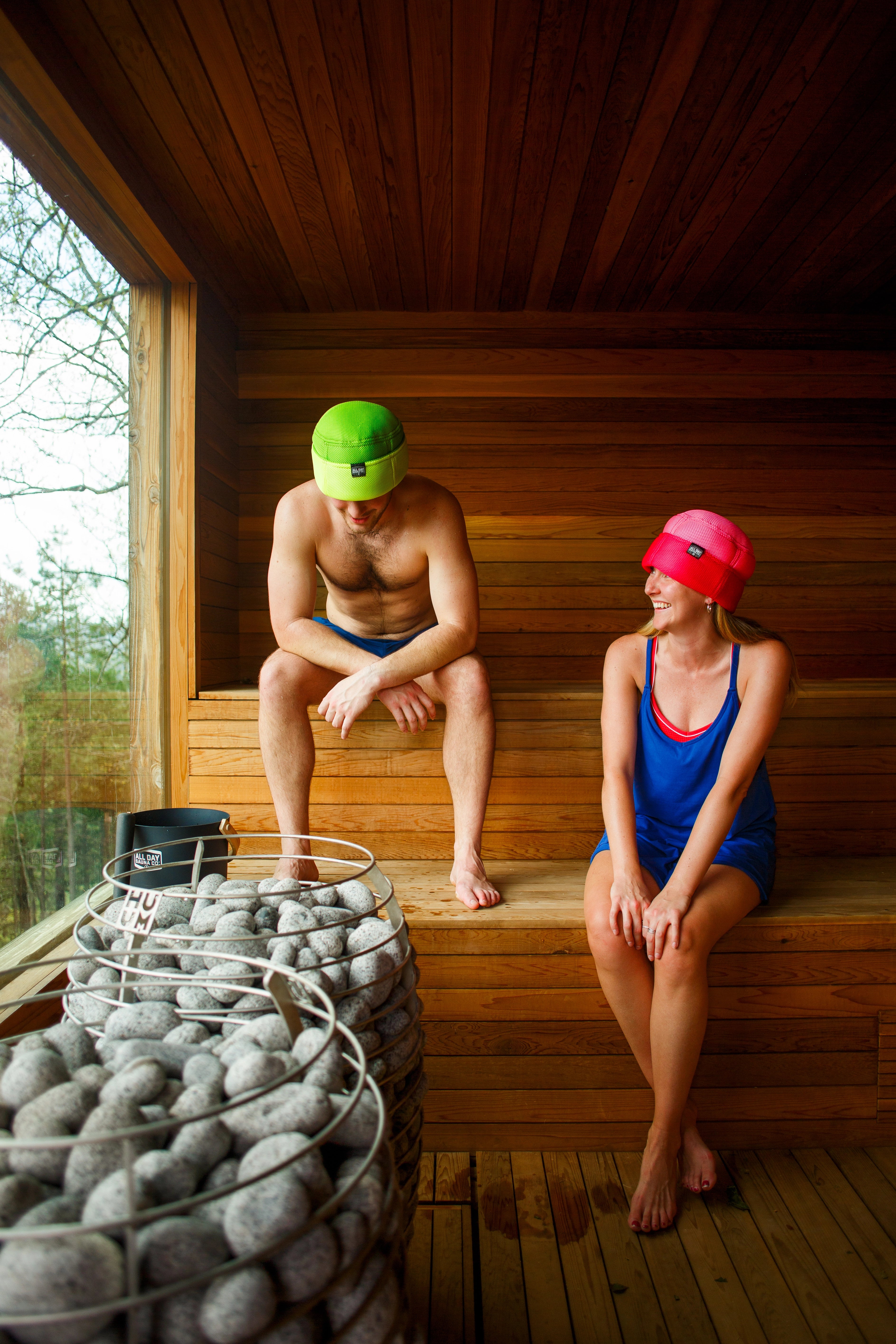 All Day Sauna Co. mesh sauna hat — breathable, machine-washable hat designed for sauna use, shown in a traditional Finnish sauna.