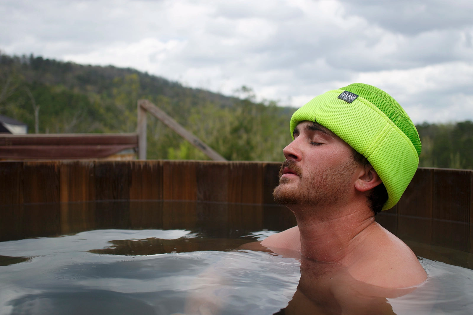 Man wearing Lime All Day Sauna Co. mesh sauna hat during outdoor sauna session — lightweight and breathable headwear for heat protection.