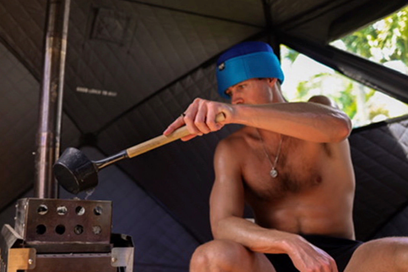 Sauna user wearing mesh sauna hat from All Day Sauna Co. while pouring water in portable outdoor sauna.
