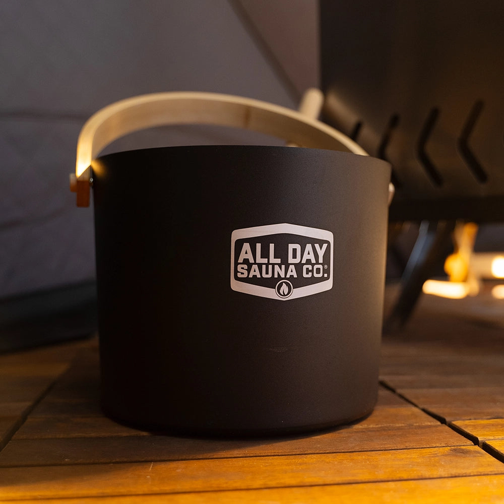 All Day Sauna Co. water bucket and ladle in active use inside sauna — adding water to hot rocks for soothing steam